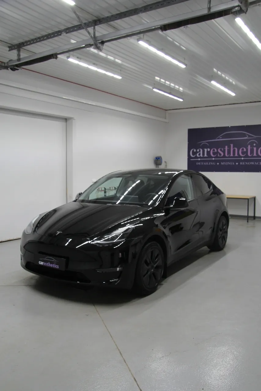 Tesla Model Y w hali studia Caresthetics pod lampami, logo na ścianie